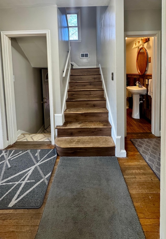 stairway featuring wood finished floors, visible vents, and baseboards