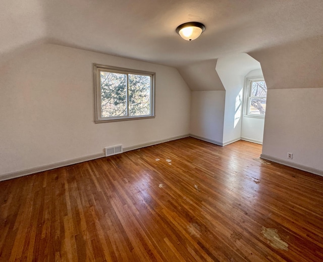 additional living space with hardwood / wood-style floors, lofted ceiling, baseboards, and visible vents