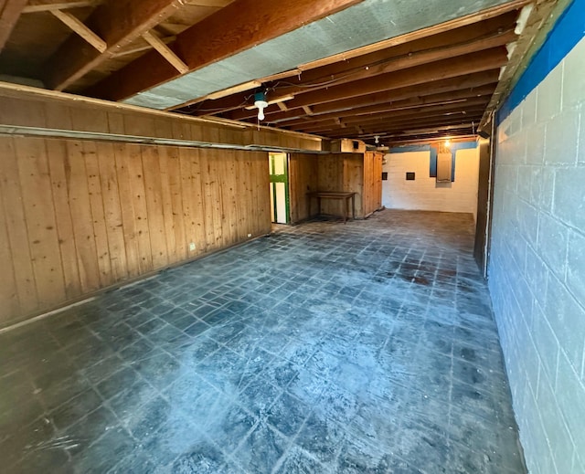 unfinished below grade area with concrete block wall, wood walls, and dark floors