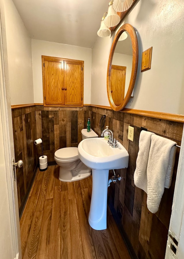 bathroom with toilet, a sink, wood finished floors, tile walls, and wainscoting