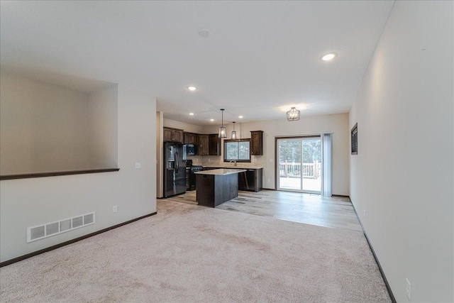 kitchen with hanging light fixtures, dark brown cabinets, black appliances, a kitchen island, and light carpet