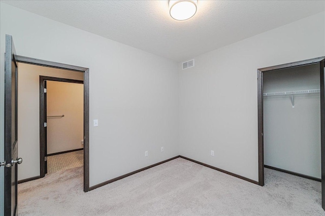 unfurnished bedroom featuring light colored carpet, a textured ceiling, and a closet