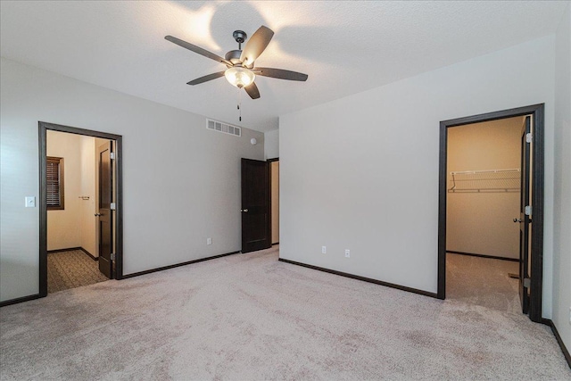 unfurnished bedroom with ceiling fan, connected bathroom, a textured ceiling, light carpet, and a spacious closet