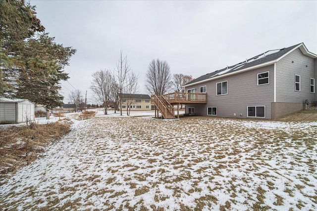 snow covered back of property with a wooden deck and a storage shed