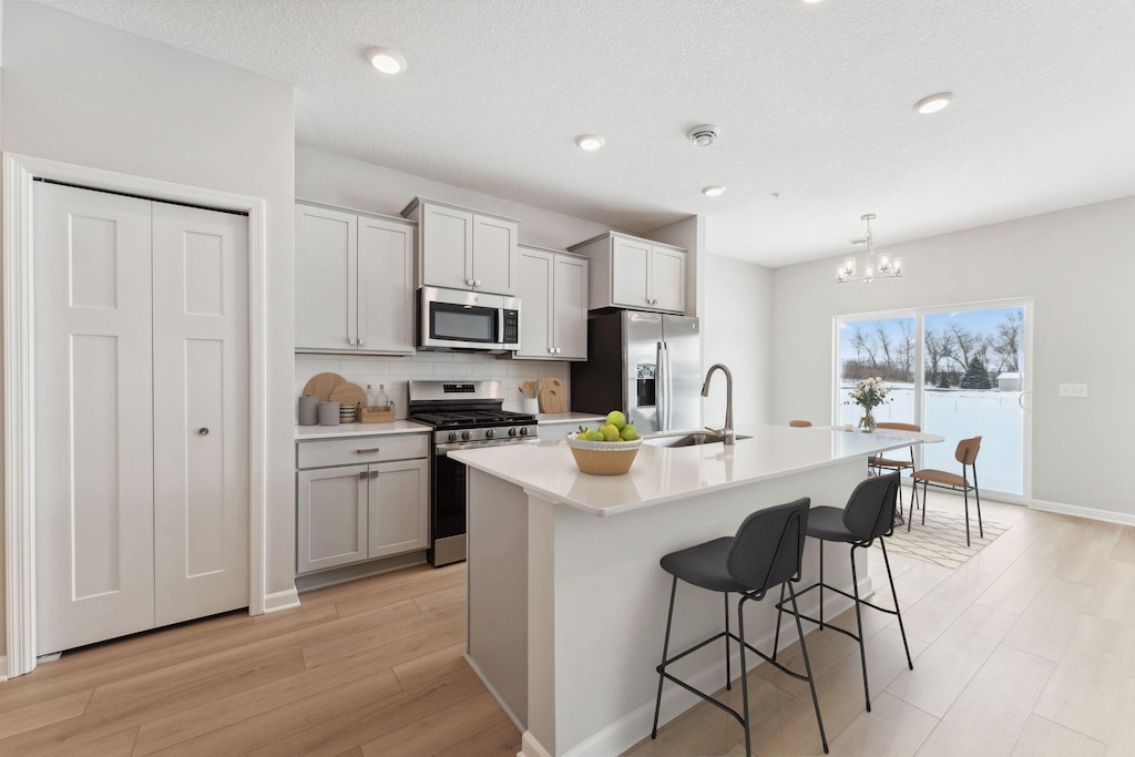 kitchen with appliances with stainless steel finishes, a kitchen island with sink, decorative light fixtures, sink, and a kitchen bar