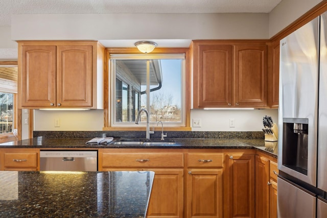 kitchen with appliances with stainless steel finishes, brown cabinetry, a sink, and dark stone countertops