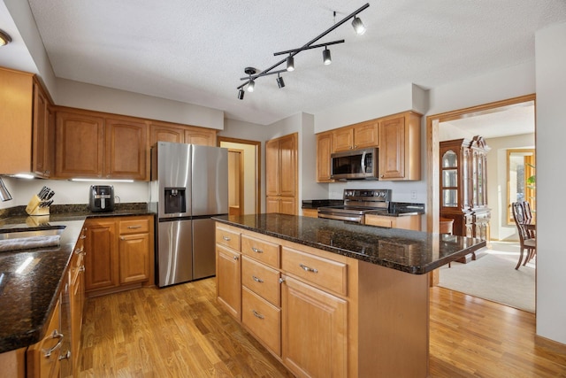 kitchen with brown cabinets, stainless steel appliances, light wood-style floors, a kitchen island, and dark stone counters