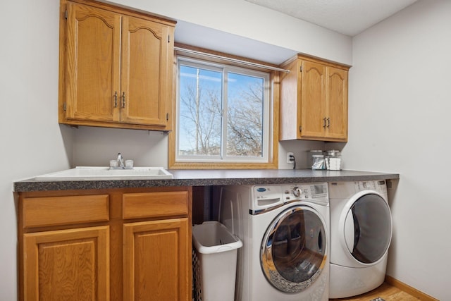 clothes washing area featuring baseboards, cabinet space, a sink, and washing machine and clothes dryer