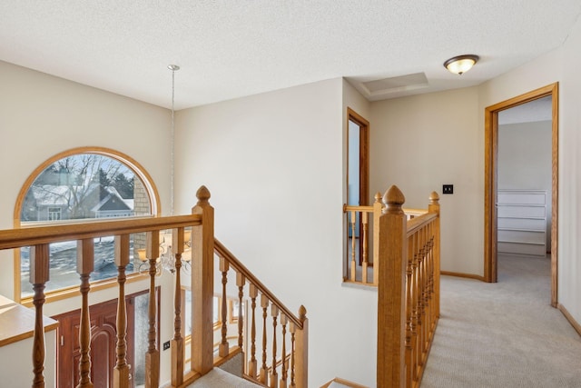 corridor with a textured ceiling, baseboards, an upstairs landing, and light colored carpet