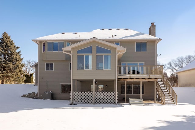 snow covered rear of property featuring a chimney, stairway, and a wooden deck