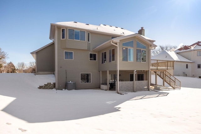 snow covered property with stairs, a deck, and a chimney