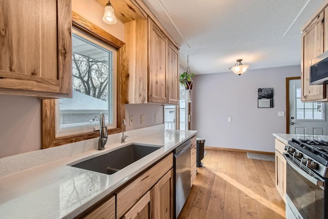 kitchen featuring appliances with stainless steel finishes, sink, light stone counters, and light wood-type flooring