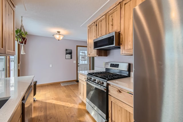 kitchen featuring appliances with stainless steel finishes, light stone counters, light brown cabinetry, and light hardwood / wood-style flooring