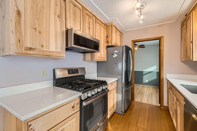 kitchen featuring stainless steel appliances, light brown cabinetry, light hardwood / wood-style flooring, and a textured ceiling