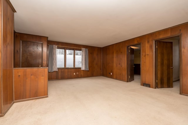 unfurnished living room featuring wooden walls and light carpet