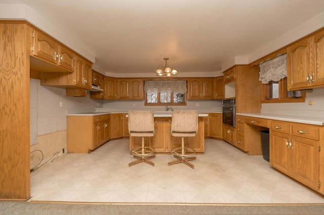 kitchen with sink, black oven, a kitchen bar, a notable chandelier, and a kitchen island