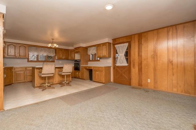 kitchen with a kitchen island, a breakfast bar, black oven, wood walls, and a chandelier