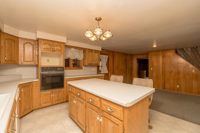 kitchen featuring black oven, hanging light fixtures, wooden walls, a center island, and a notable chandelier