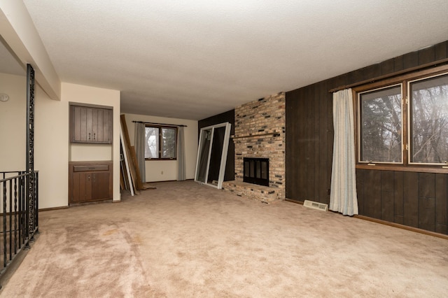 unfurnished living room featuring a brick fireplace, light colored carpet, a textured ceiling, and wood walls