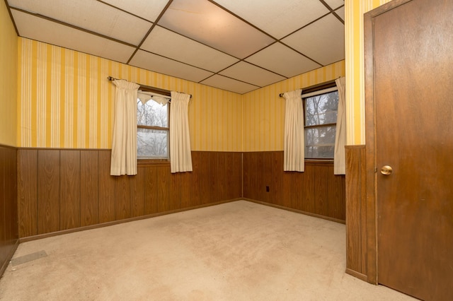 empty room featuring a paneled ceiling, light colored carpet, and wood walls