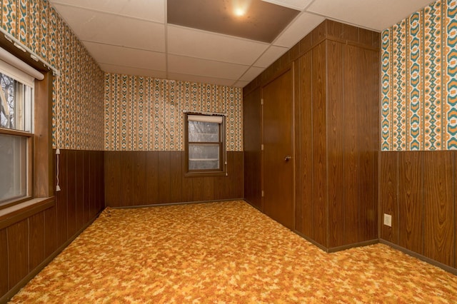 empty room featuring carpet floors, a paneled ceiling, and wooden walls