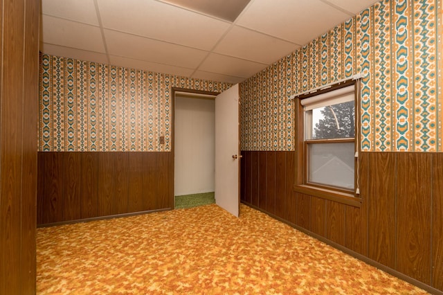 empty room featuring wooden walls and a drop ceiling