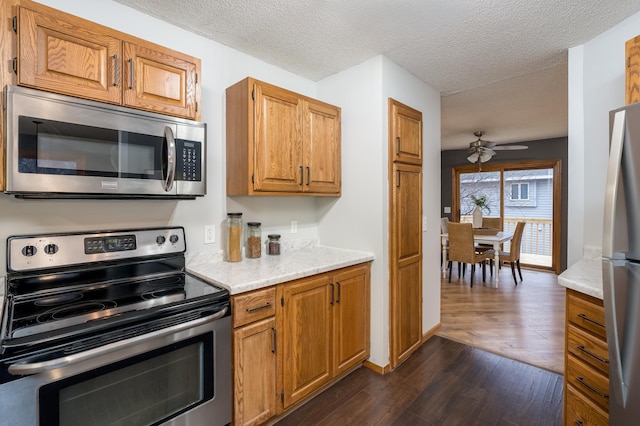 kitchen with dark wood-type flooring, ceiling fan, stainless steel appliances, and a textured ceiling