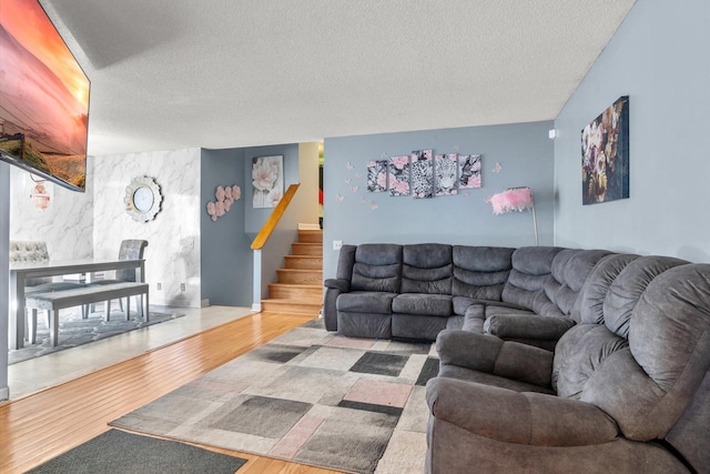 living room with stairway, a textured ceiling, wood finished floors, and an accent wall