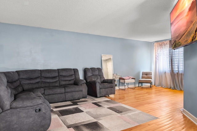 living room with light wood-type flooring, baseboards, and a textured ceiling