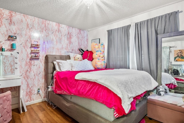 bedroom with baseboards, a textured ceiling, wood finished floors, and wallpapered walls