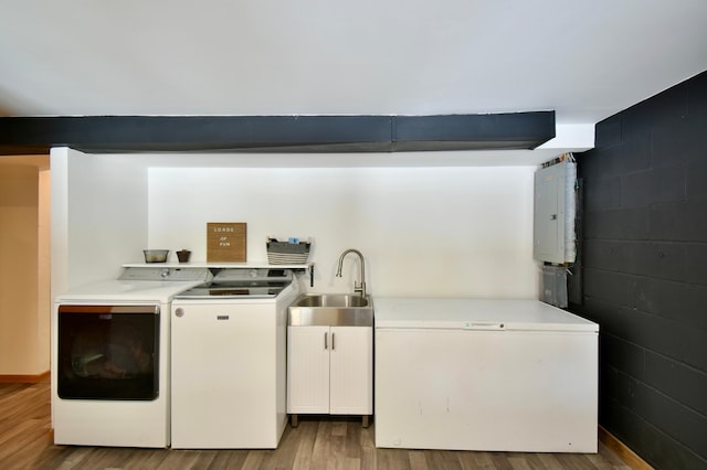 laundry room with cabinet space, electric panel, light wood-style flooring, washer and dryer, and a sink