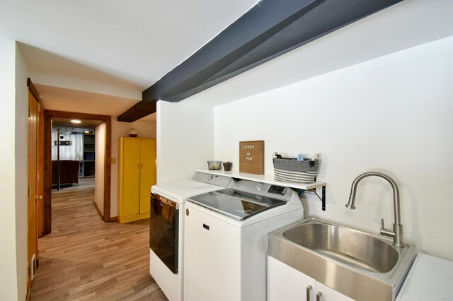 clothes washing area with cabinet space, light wood-style flooring, washer and clothes dryer, and a sink