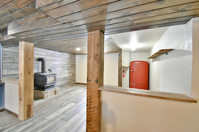 finished basement with a wood stove, baseboards, wood walls, and light wood finished floors