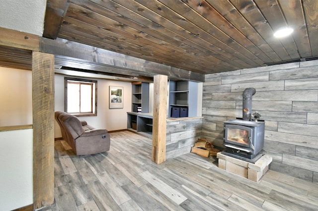 living area featuring baseboards, wooden ceiling, wood finished floors, a wood stove, and wood walls