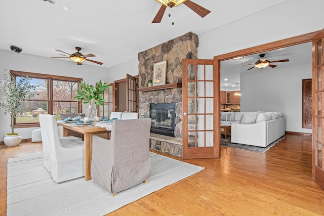 dining room with ceiling fan, a stone fireplace, and light hardwood / wood-style floors