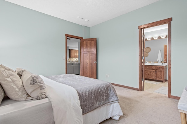 bedroom featuring ensuite bath, light carpet, and a textured ceiling