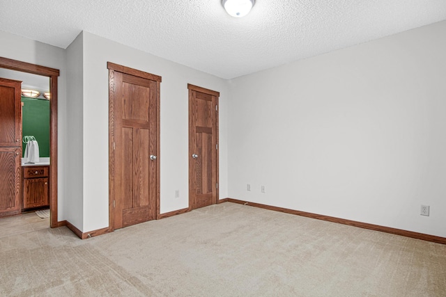 unfurnished bedroom featuring connected bathroom, light carpet, and a textured ceiling