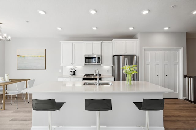 kitchen with white cabinetry, stainless steel appliances, sink, and a large island with sink