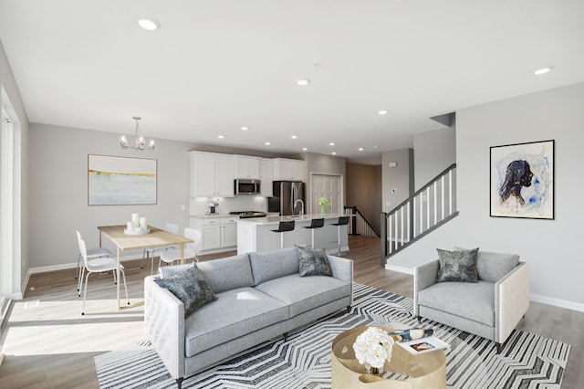 living room featuring light wood finished floors, recessed lighting, an inviting chandelier, baseboards, and stairs