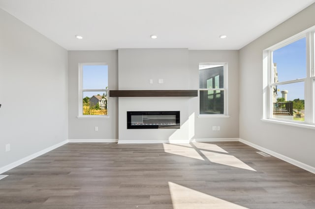 unfurnished living room featuring light wood finished floors, recessed lighting, a glass covered fireplace, and baseboards