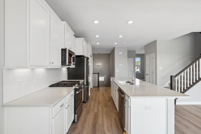 kitchen with stainless steel appliances, light countertops, white cabinets, a kitchen island with sink, and a sink