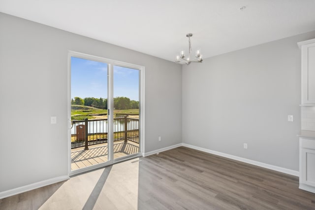 empty room featuring a chandelier, a water view, baseboards, and wood finished floors