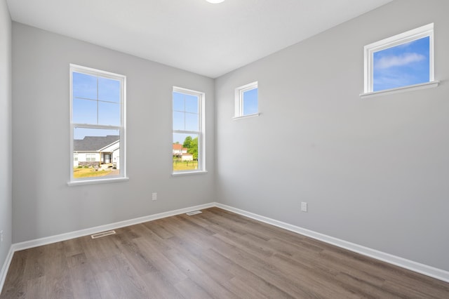 empty room with light wood finished floors, baseboards, and visible vents