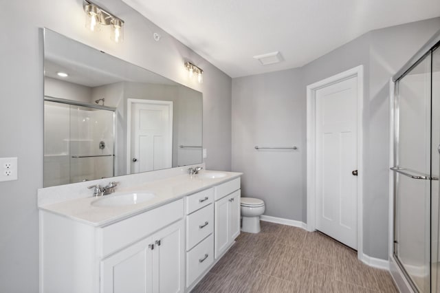 full bathroom featuring double vanity, a shower stall, baseboards, and a sink