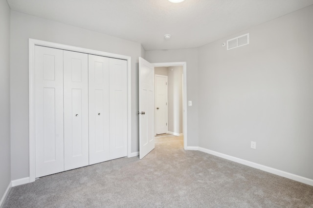 unfurnished bedroom with light colored carpet, a closet, visible vents, and baseboards