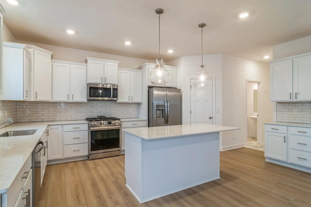 kitchen featuring appliances with stainless steel finishes, decorative light fixtures, sink, white cabinets, and light wood-type flooring