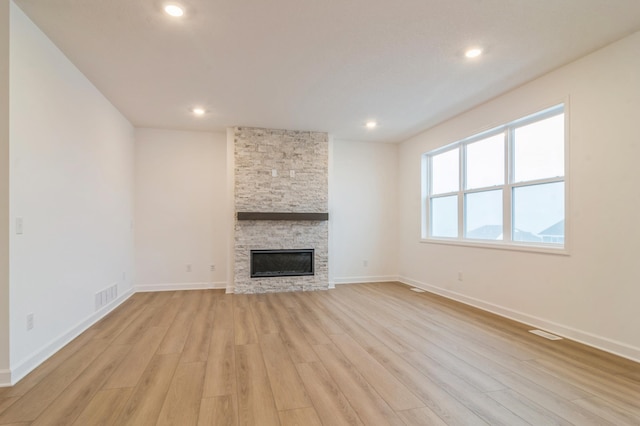 unfurnished living room with a stone fireplace and light hardwood / wood-style floors