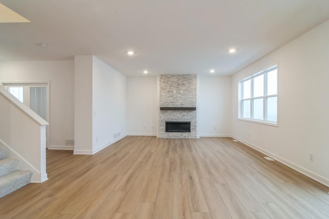 unfurnished living room featuring a stone fireplace and light wood-type flooring