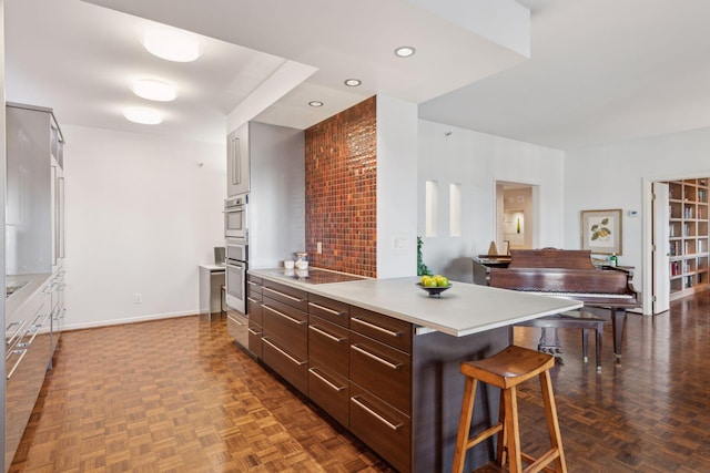 kitchen featuring dark brown cabinetry, a kitchen bar, stainless steel double oven, and dark parquet flooring