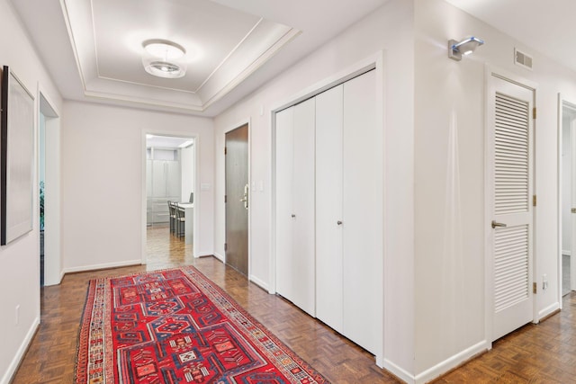 hallway featuring a tray ceiling and dark parquet flooring